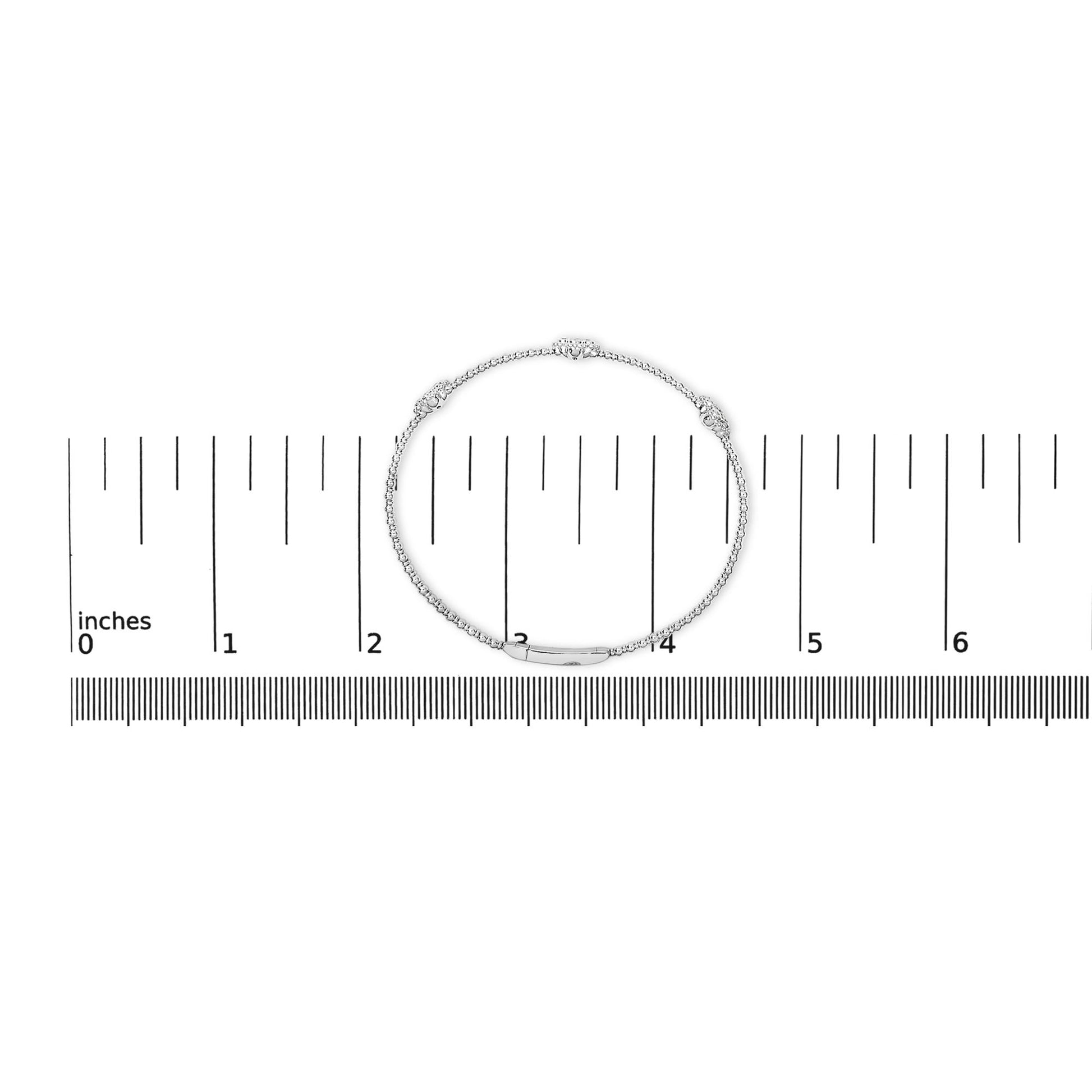 White bracelet with round white gemstones in shared prong settings, shown lying flat on a ruler for scale, top-down angle.