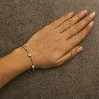 Yellow bracelet with small flower-shaped clusters of white gemstones along a delicate chain, shown worn on a model's wrist from a top-down angle.