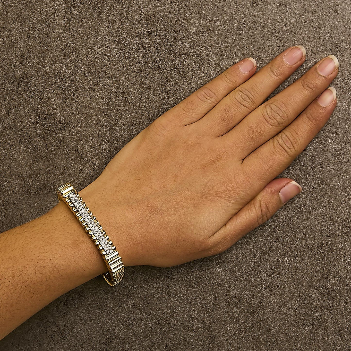 Yellow bracelet with a central panel of white round pave gemstones shown on a model's wrist, top-down angle.