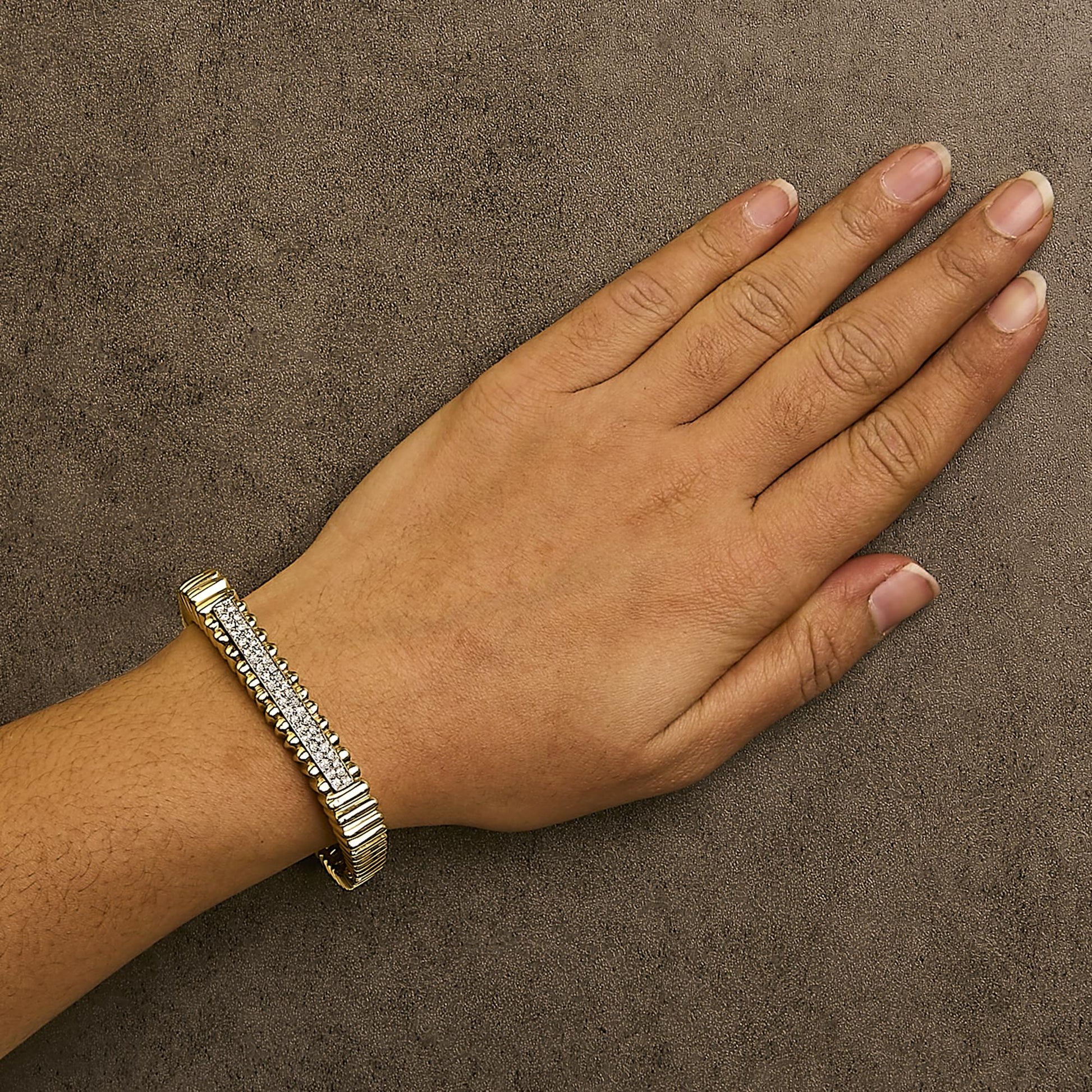 Yellow bracelet with a central panel of white round pave gemstones shown on a model's wrist, top-down angle.