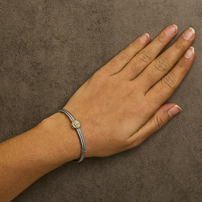 Bracelet shown worn on a model's wrist, featuring a two-tone band with a round yellow centerpiece set with one bezel-set white gemstone and multiple prong-set white gemstones, viewed from above at an angle.