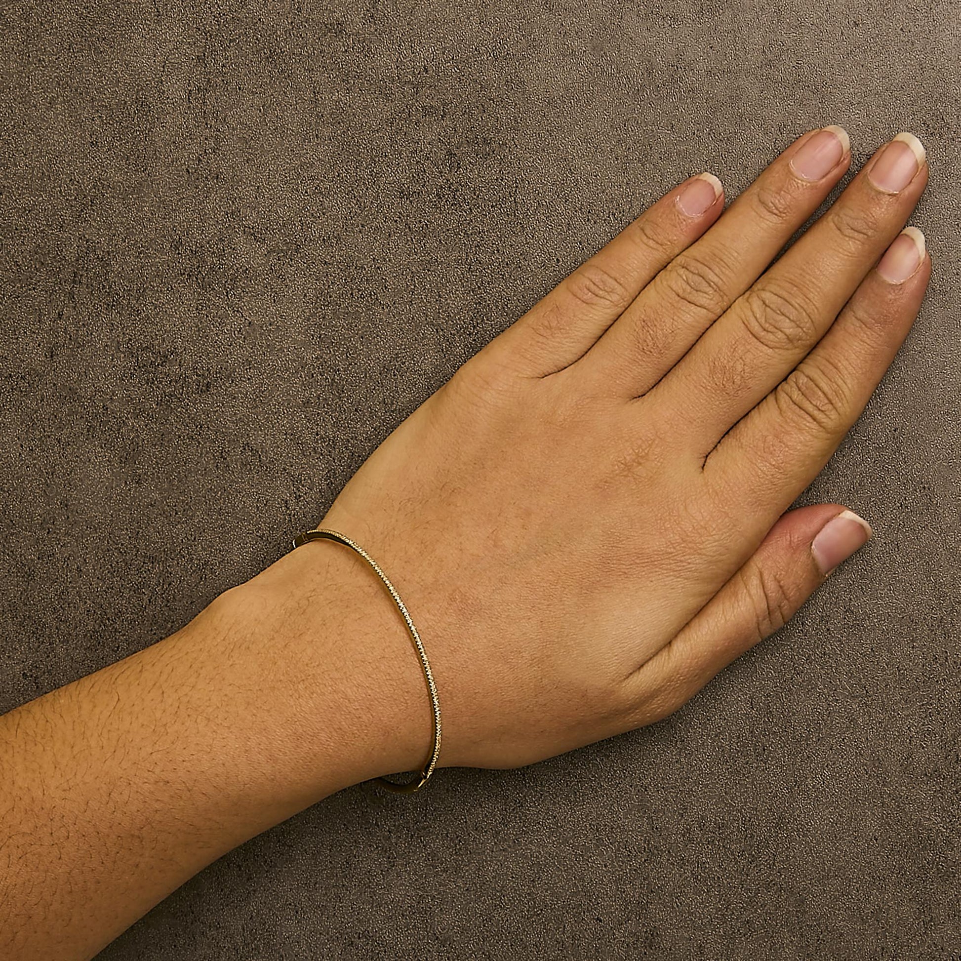 Bracelet with round white gemstones in prong setting on yellow metal, shown worn on a model's wrist, top-down angle.