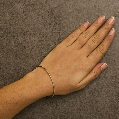 Bracelet with round white gemstones in prong setting on yellow metal, shown worn on a model's wrist, top-down angle.