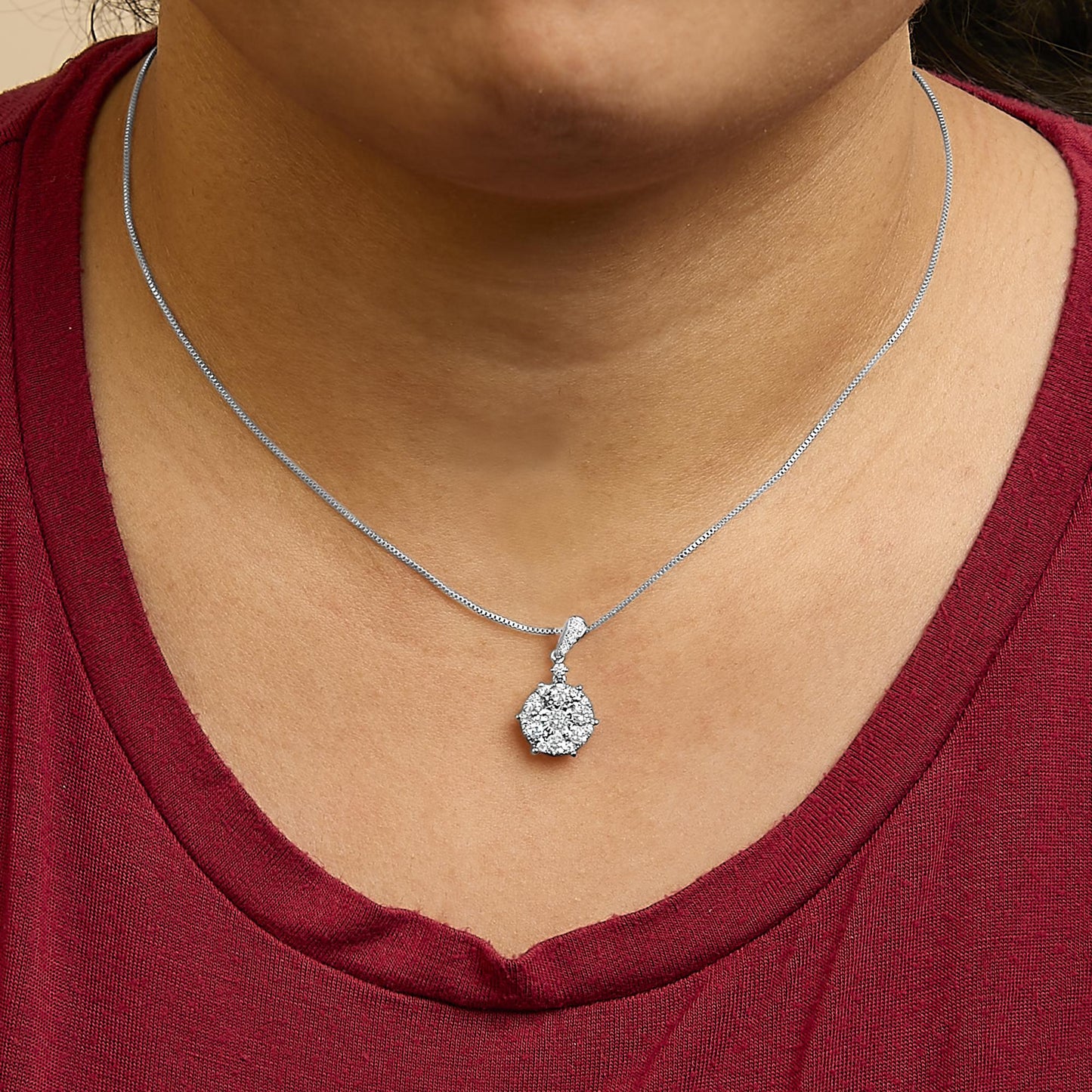 Close-up front view of a white metal necklace with a round cluster pendant featuring a central white gemstone in a miracle setting surrounded by smaller white gemstones in shared prong and prong settings, shown worn on a model.