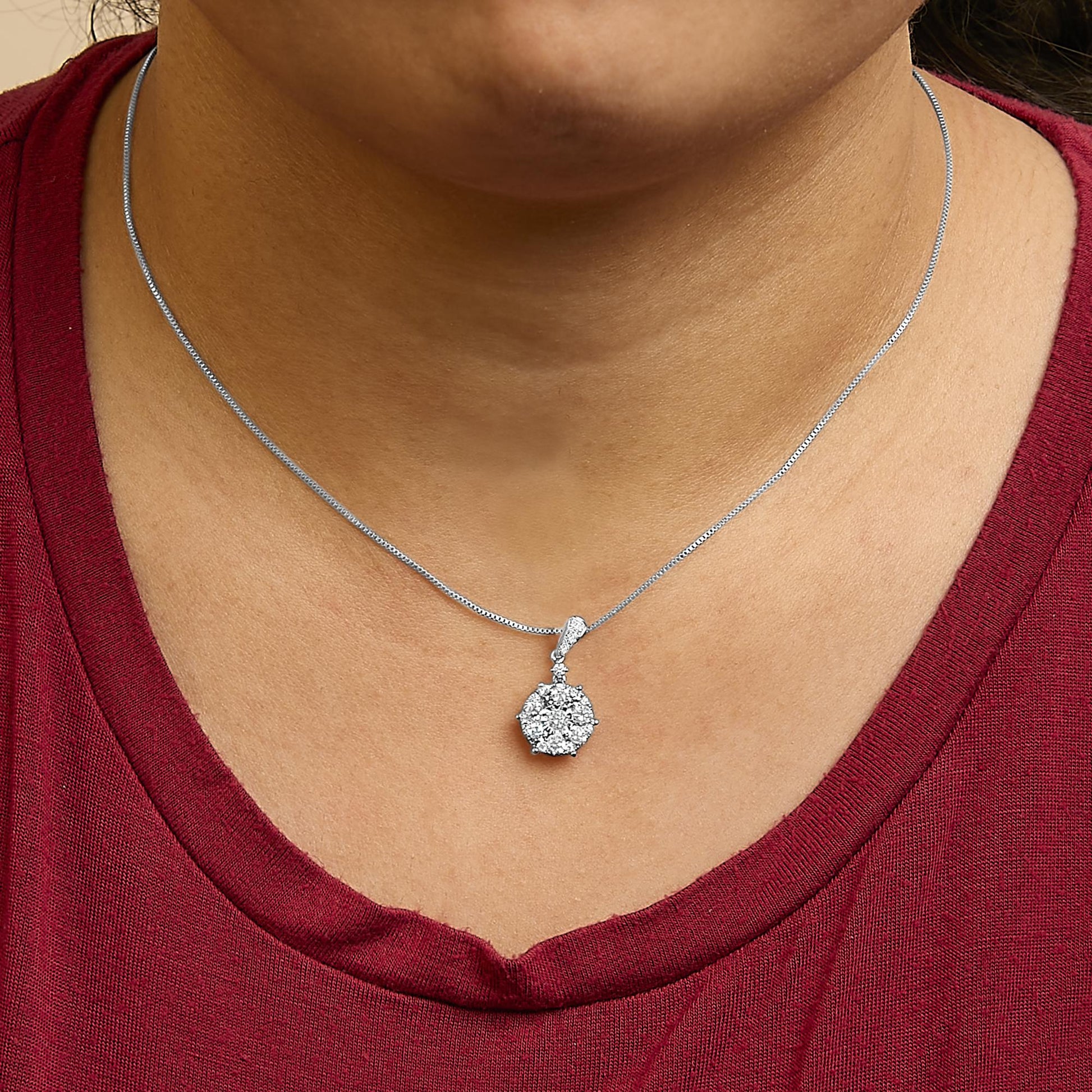 Close-up front view of a white metal necklace with a round cluster pendant featuring a central white gemstone in a miracle setting surrounded by smaller white gemstones in shared prong and prong settings, shown worn on a model.