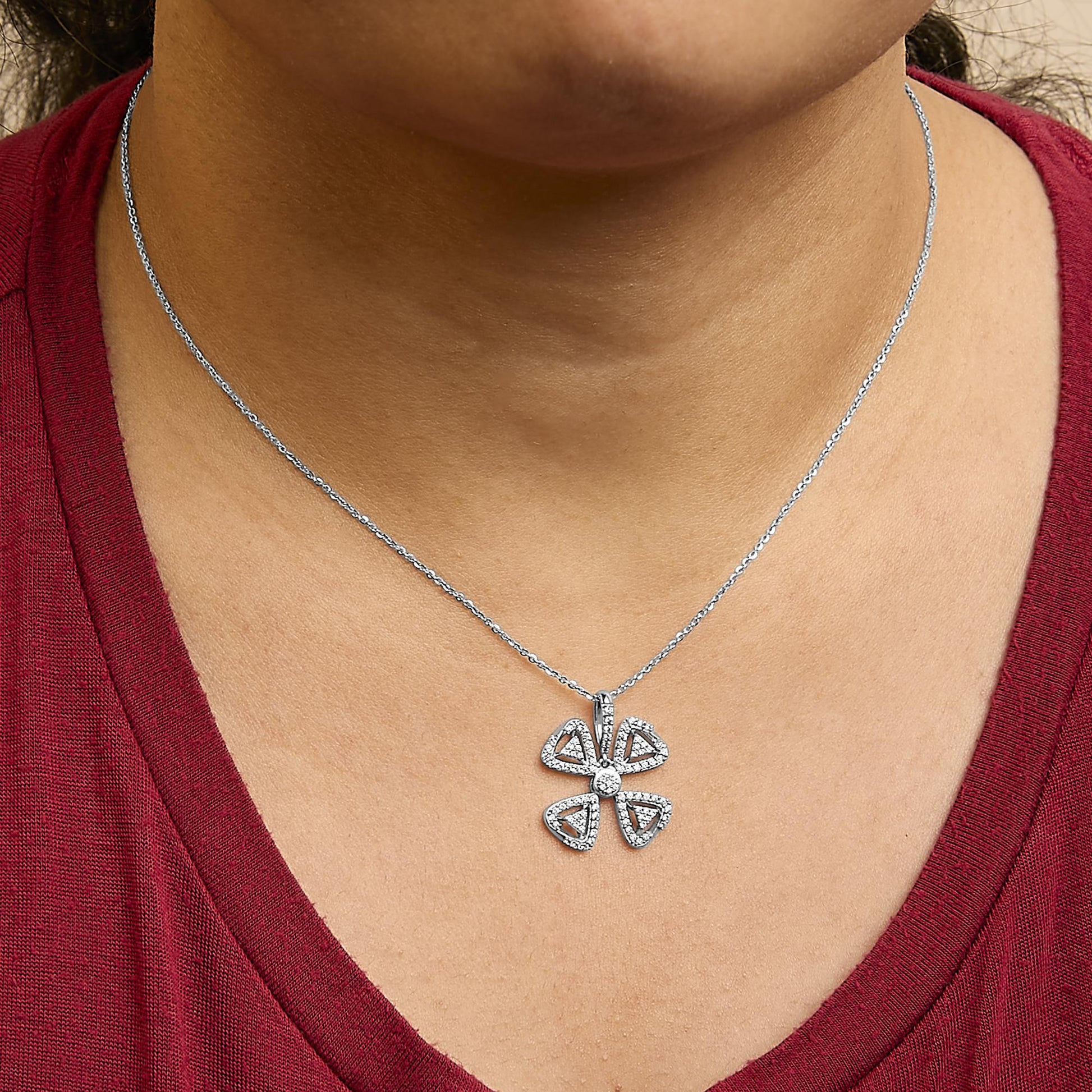 White metal necklace with a floral-shaped pendant featuring four triangular sections and a round center, all adorned with small white gemstones, shown worn on a model in a close-up front view.