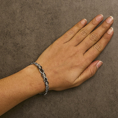 White metal bracelet with intertwined oval links featuring alternating black and white round gemstones in shared prong settings, shown worn on a model's wrist from top angle.