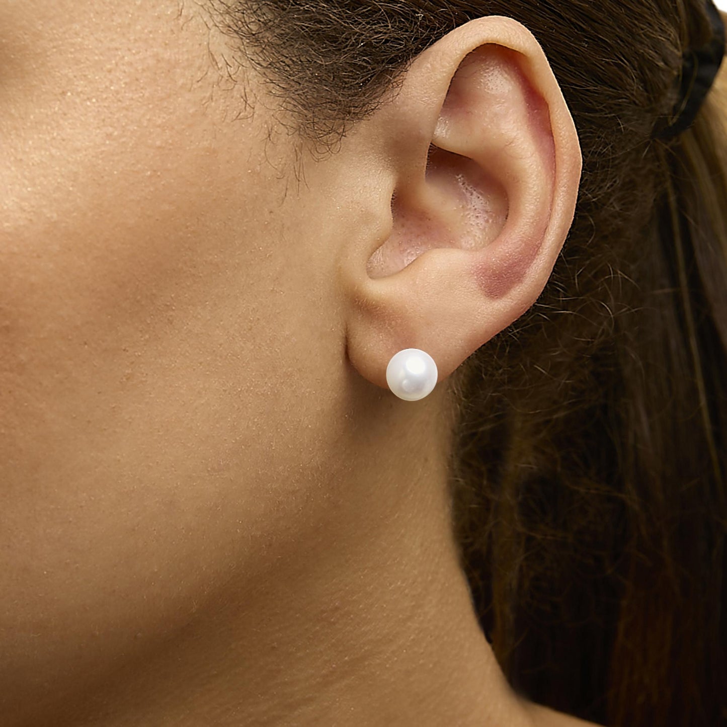 Close-up side view of a model wearing a single round white gemstone stud earring with yellow metal setting.