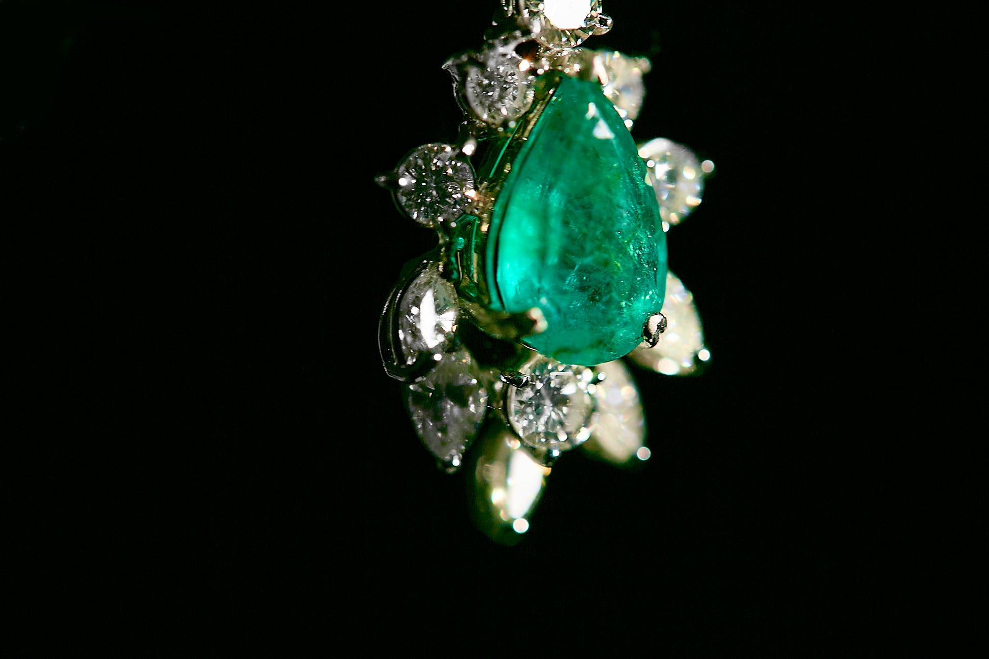 Close-up front angle of a piece from a white metal jewelry set featuring a large pear-shaped green gemstone in the center, surrounded by various round and marquise-shaped white gemstones.