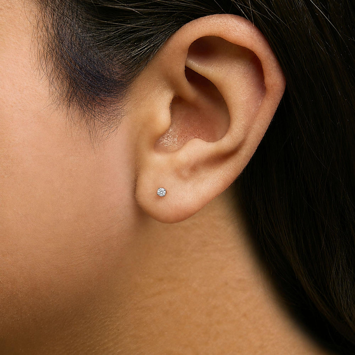 Close-up side angle of a model wearing a white metal stud earring with a round white gemstone in a 4-prong setting.