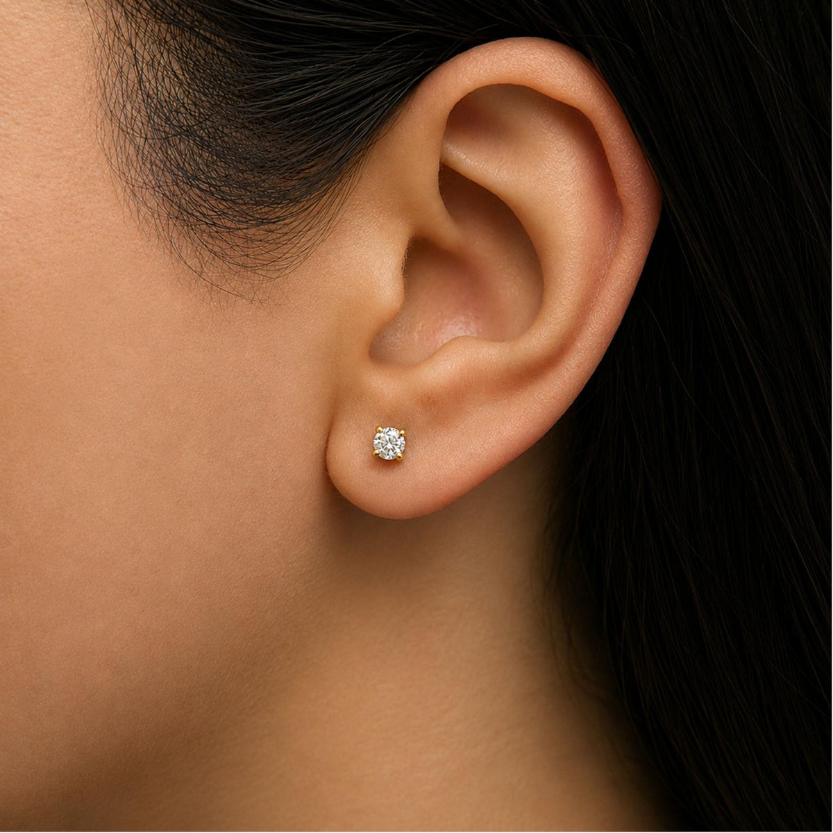 Close-up side view of a model wearing a yellow metal earring with a round white gemstone in a 4-prong setting.