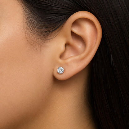 Close-up side view of a model's ear wearing a white metal earring with a round white gemstone set in a four-prong setting.
