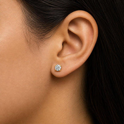 Close-up side view of a model wearing a pair of yellow metal stud earrings with round white gemstones in 4-prong settings.