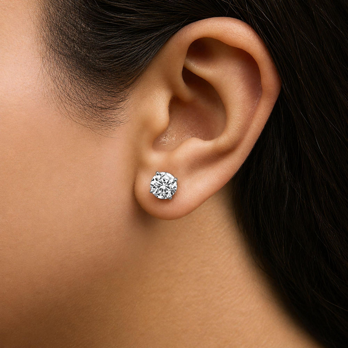 Close-up side view of a model wearing white stud earrings with round cut white gemstones set in a 4-prong setting.