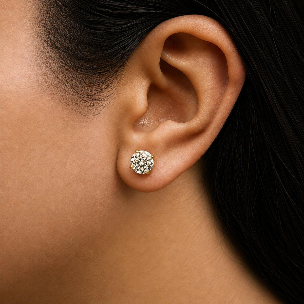 Close-up side view of a model wearing yellow metal stud earrings with round white gemstones in 4-prong settings.