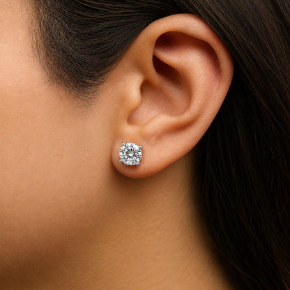 Close-up side view of a white metal stud earring with a round white gemstone in a four-prong setting, shown worn on a model's ear.