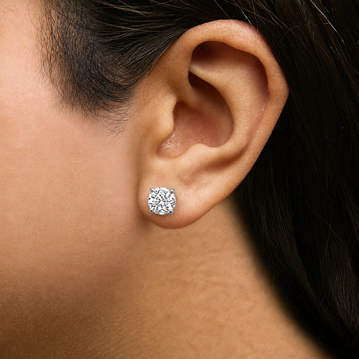 Close-up side view of a model wearing a white metal earring with a single round white gemstone in a four-prong setting.