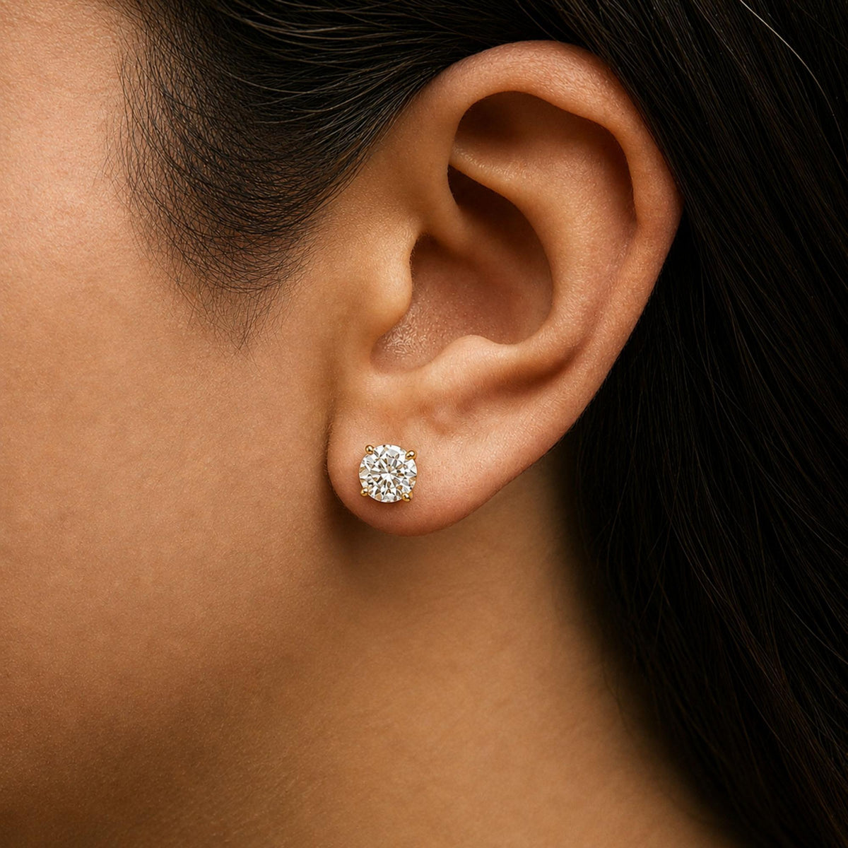 Close-up side view of a model wearing a yellow metal earring featuring a round white gemstone in a 4-prong setting.