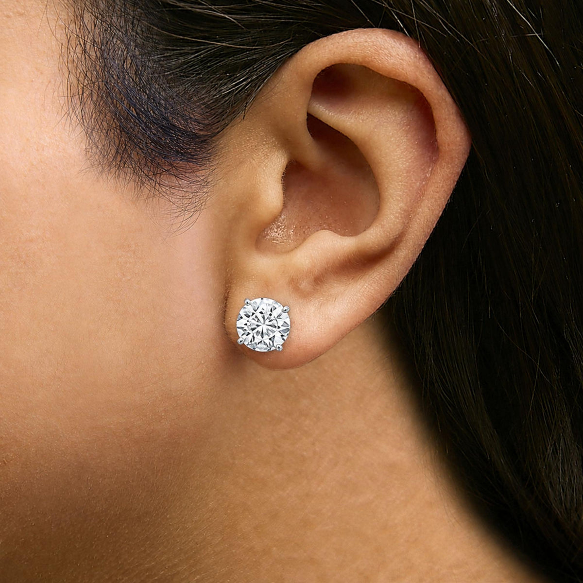 Close-up side view of a model wearing a white metal earring with a round white gemstone in a 4-prong setting.