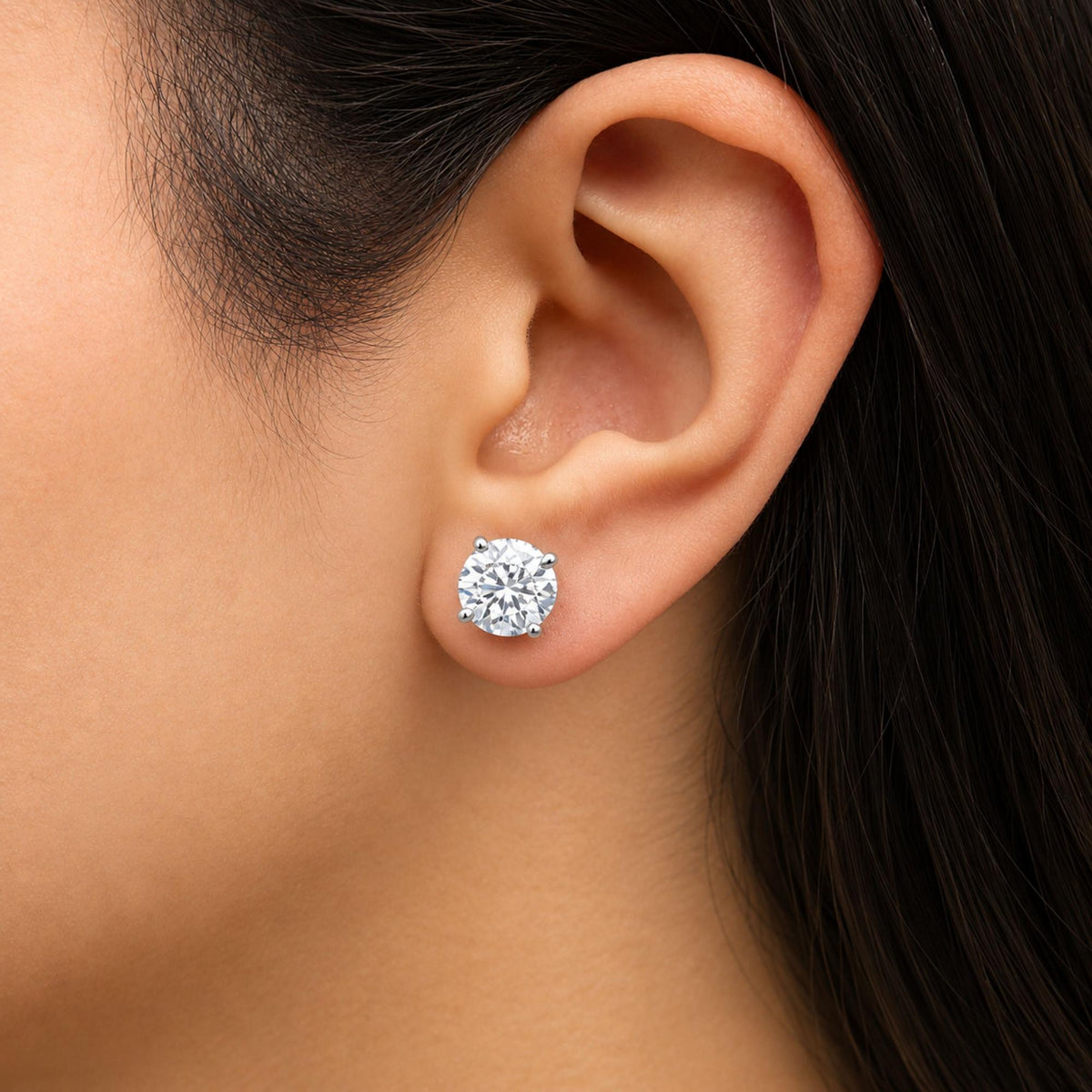 Close-up side view of a model's ear wearing a white metal stud earring featuring a round white gemstone in a 4-prong setting.