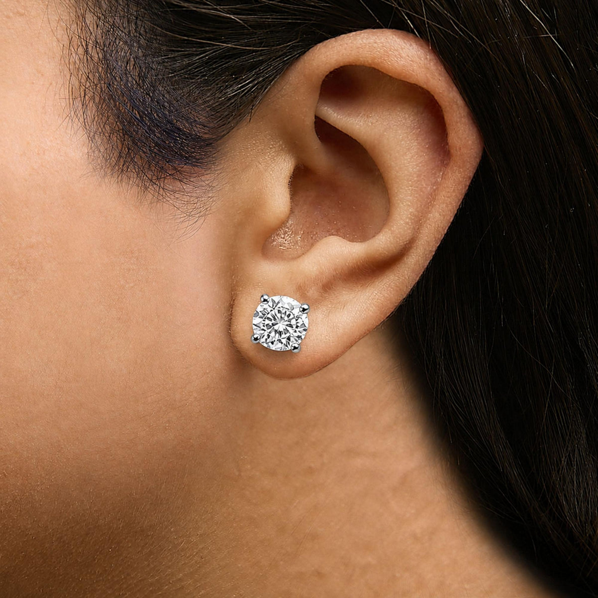 Close-up front angle of a model wearing white metal stud earrings with round white gemstones in 4-prong settings.