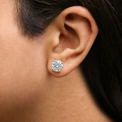 Close-up side view of a yellow metal earring with a round white gemstone in a four-prong setting, shown worn on a model's ear.
