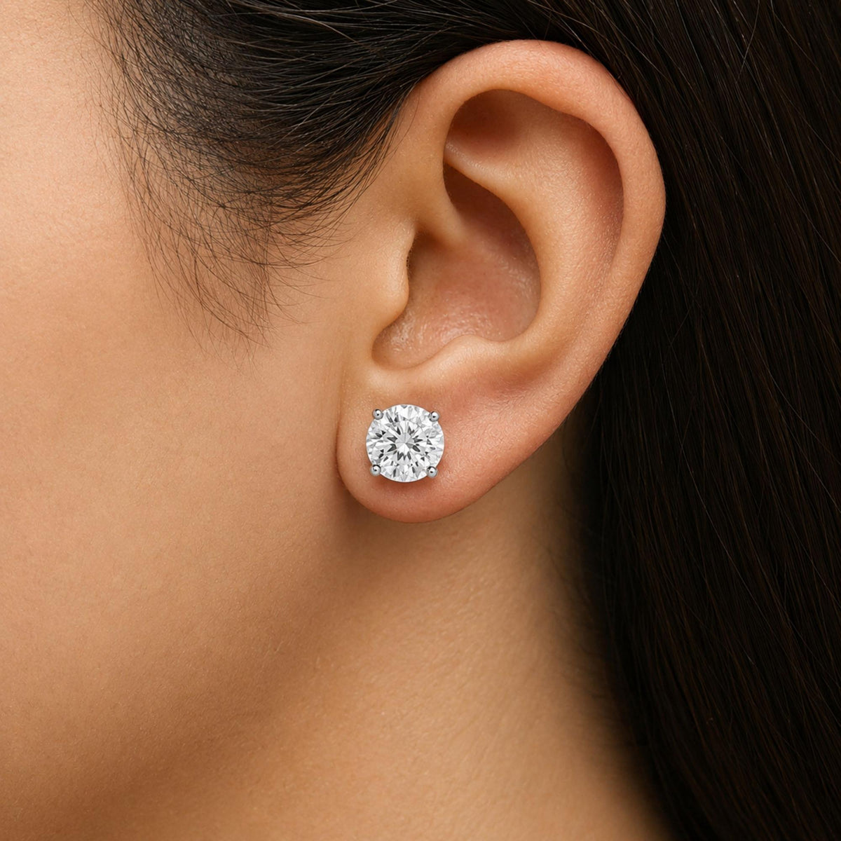Close-up side view of a model wearing a single white metal stud earring set with a round white gemstone in a 4-prong setting.