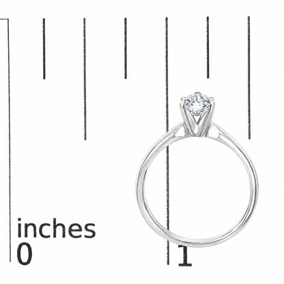 Close-up front view of a white metal ring with a round white gemstone in a 4-prong setting, shown on a scale.