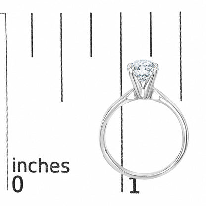 Close-up front angle of a white metal ring with a round white gemstone in a 4-prong setting shown on a measurement scale.