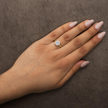 Yellow ring with a round white gemstone in a four-prong setting shown worn on a model's left hand, angled top-down.