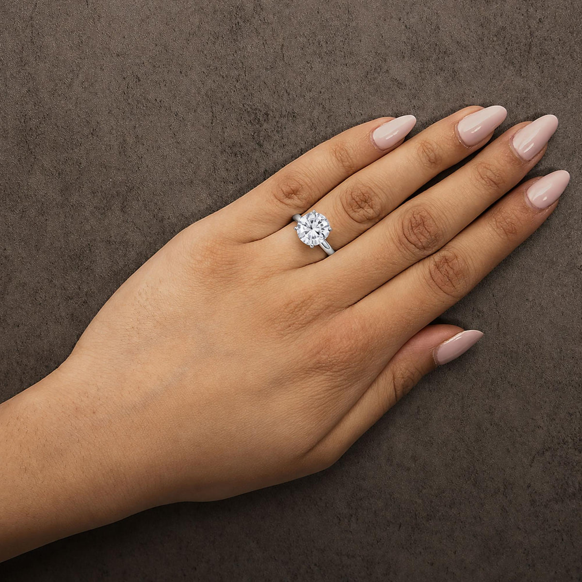 White metal ring with a round white gemstone in a four-prong setting, shown worn on a model's hand from a top-down angle.