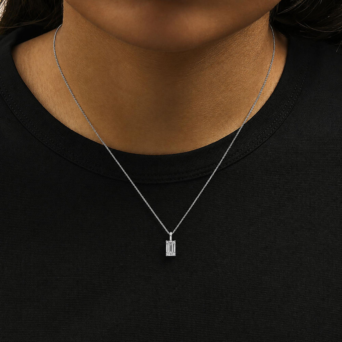 Close-up frontal shot of a model wearing a white metal necklace with a rectangular emerald-shaped white gemstone pendant in a four-prong setting.