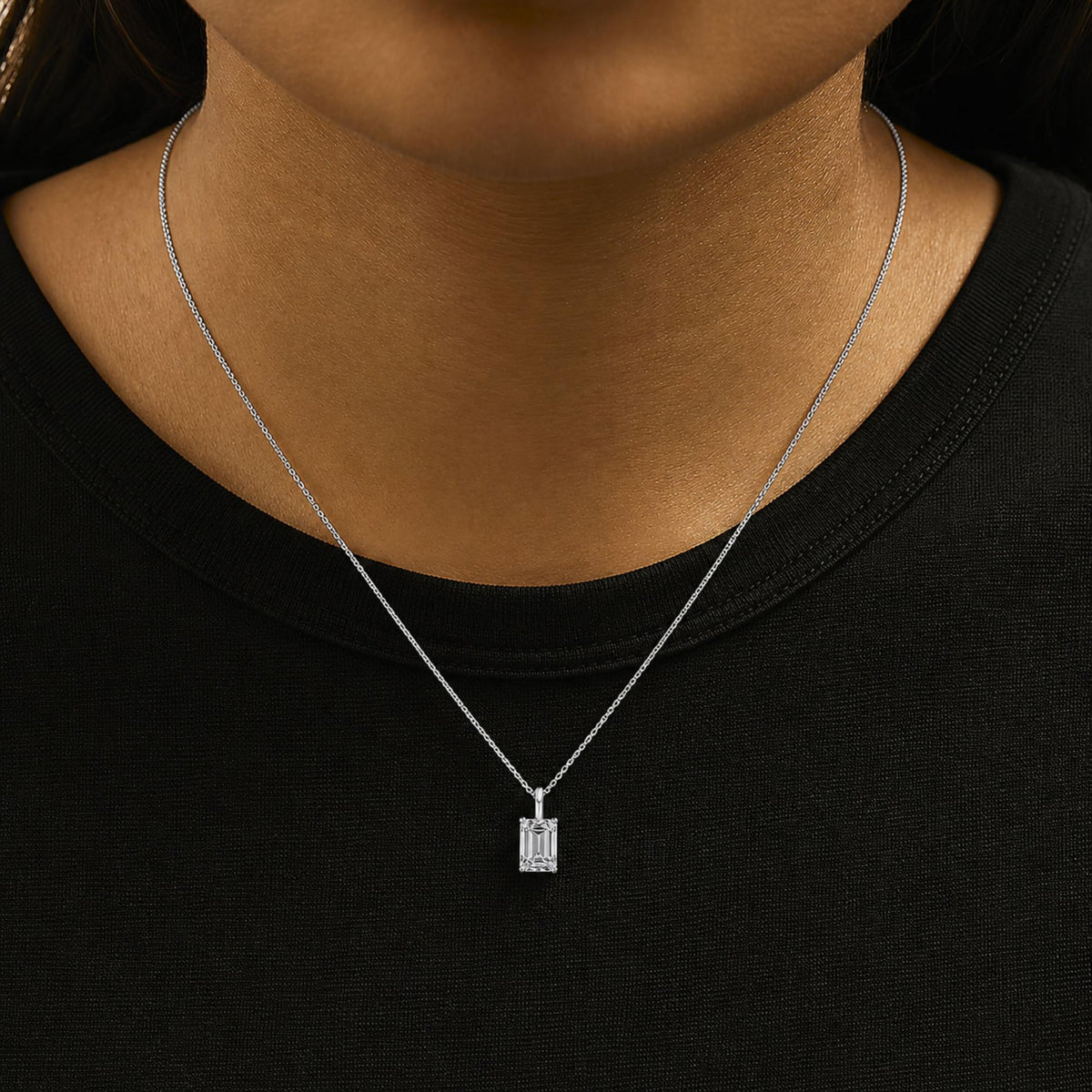 Close-up front view of a white necklace with an emerald-shaped white gemstone pendant in a 4-prong setting, shown worn on a model.