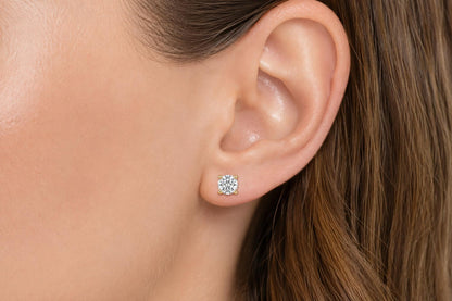 Close-up side view of a model wearing a yellow metal stud earring with a round white gemstone in a four-prong setting.