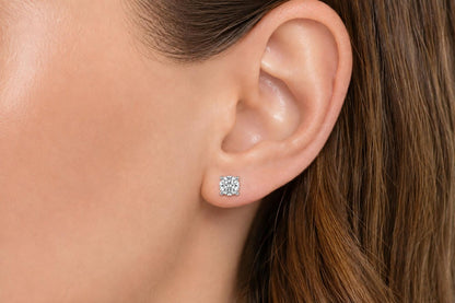 Close-up side view of a model wearing white metal stud earrings with round white gemstones in a four-prong setting.