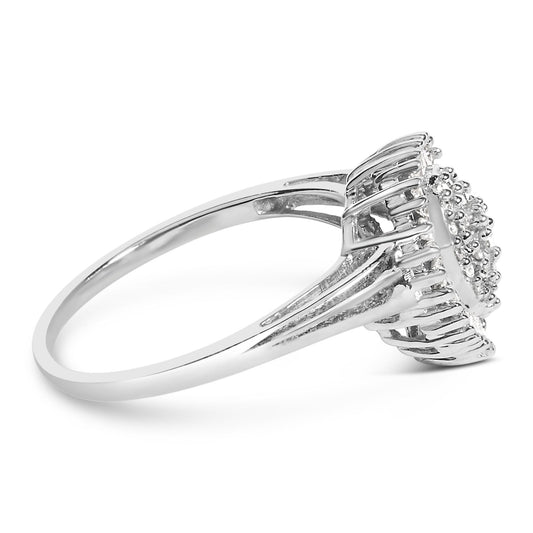 Side angle view of a white metal ring with a raised cluster of round white gemstones in prong settings surrounded by a frame of baguette-shaped white gemstones in channel settings.