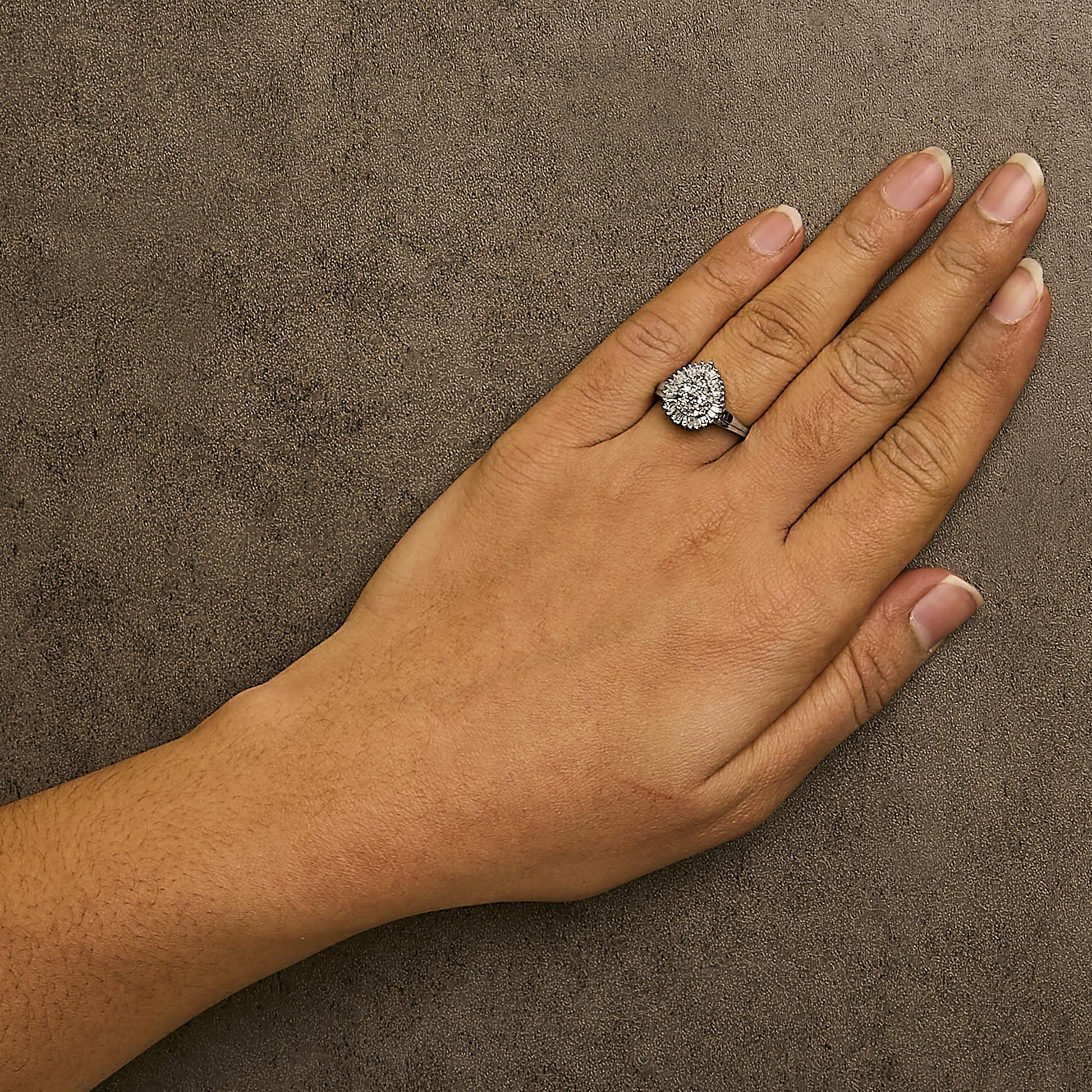 White metal ring with round and baguette shaped white gemstones in prong and channel settings, worn on a model's hand, shown from above angle.