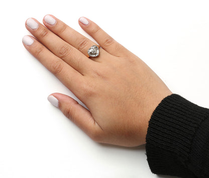 Yellow metal ring with heart-shaped cluster of white round and baguette gemstones, worn on hand, shot from above at an angle.