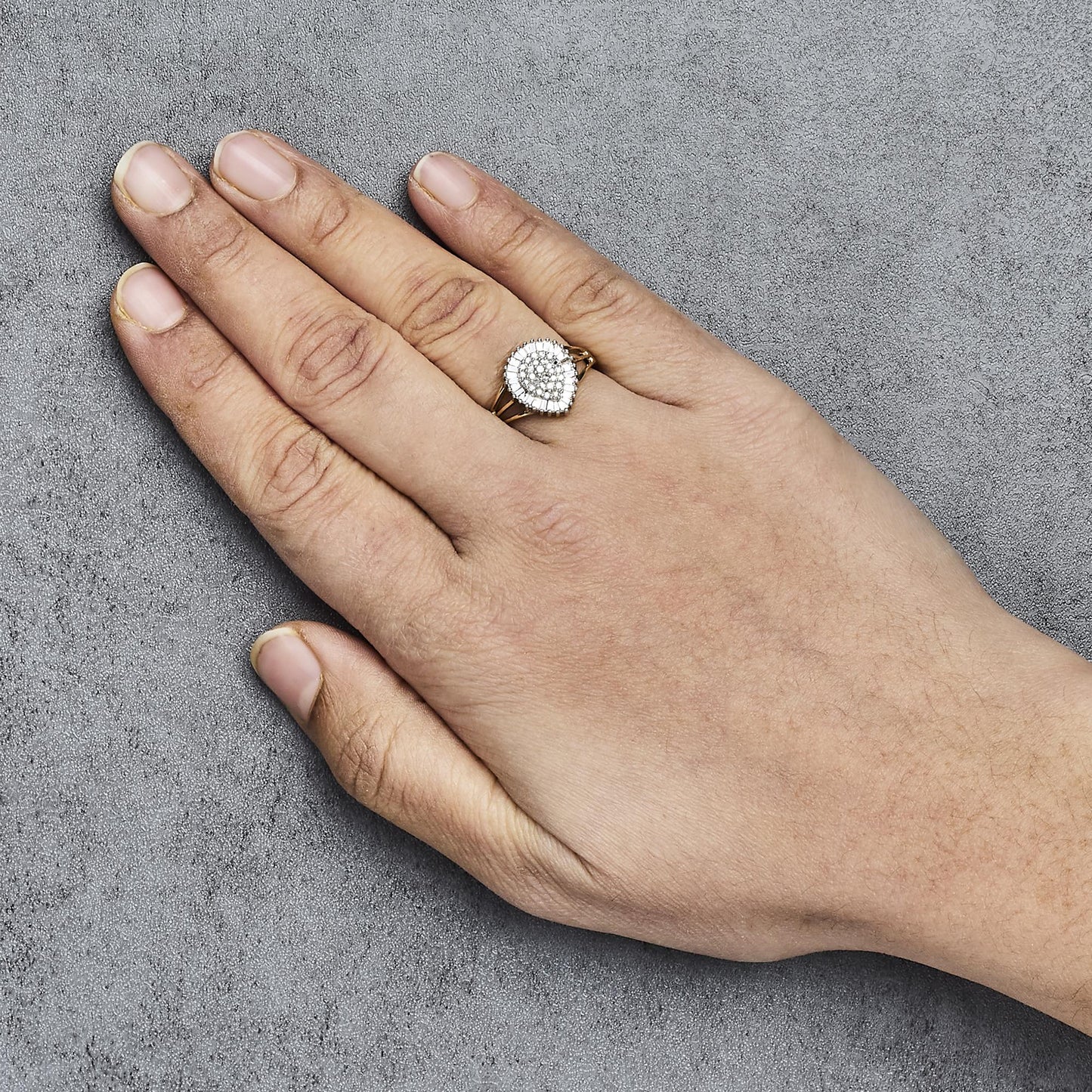 Yellow metal ring with pear-shaped cluster of white round gemstones in prong setting, surrounded by white baguette gemstones in channel setting, shown on a model's hand from top angle.