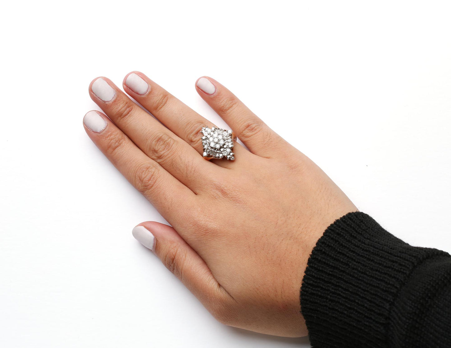 Close-up top view of a yellow metal ring on a model's finger, featuring multiple round and baguette-shaped white gemstones in prong settings.