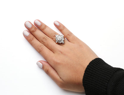Close-up top view of a yellow metal ring on a model's finger, featuring multiple round and baguette-shaped white gemstones in prong settings.