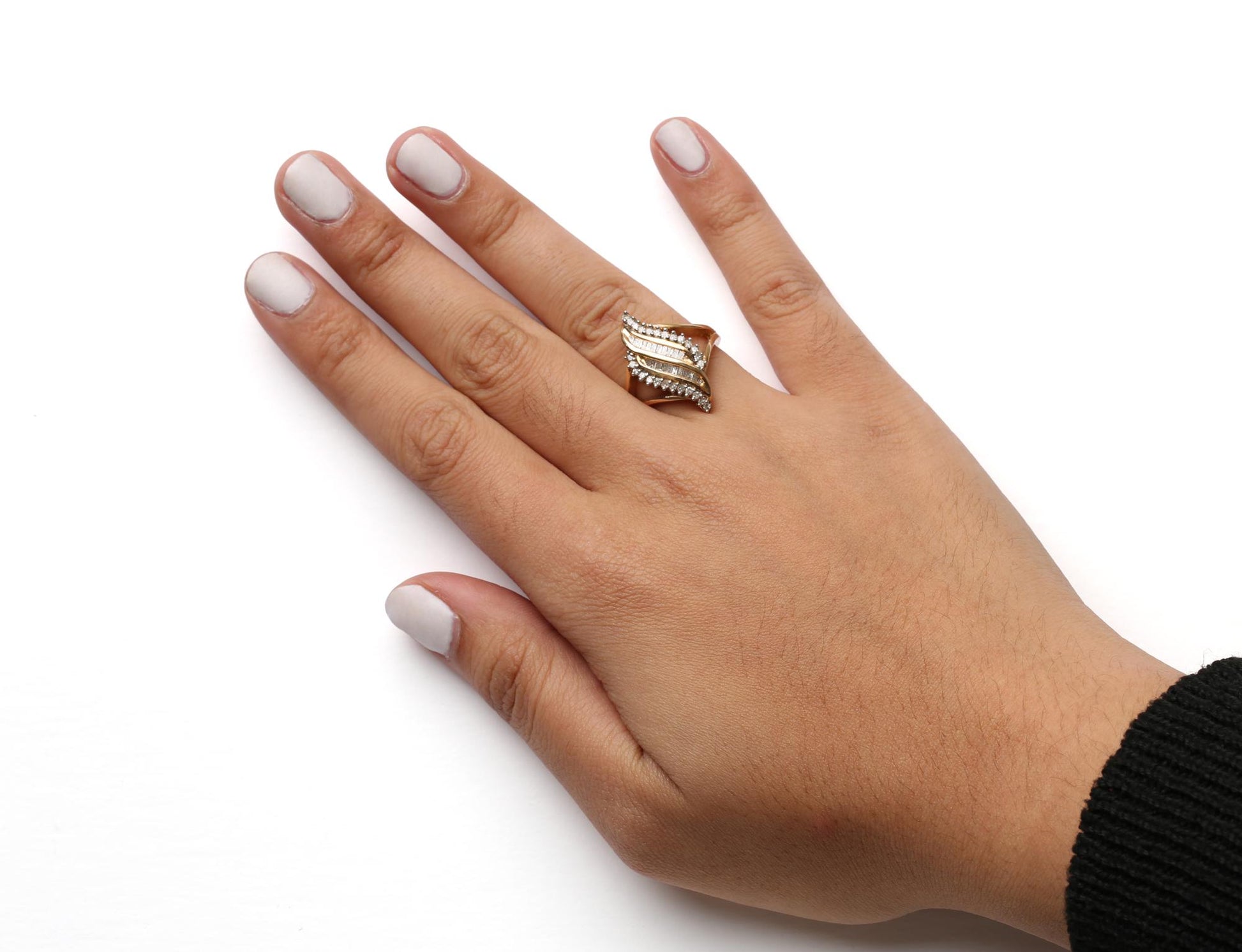 Close-up of a yellow metal ring with white round prong-set gemstones and white baguette channel-set gemstones, worn on a model's hand, shot from above.