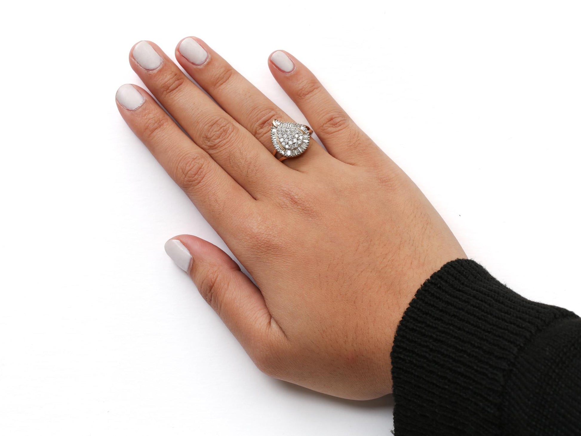 Close-up of a yellow metal ring with round and baguette-shaped white gemstones in prong settings, worn on a model's hand, shot from above.