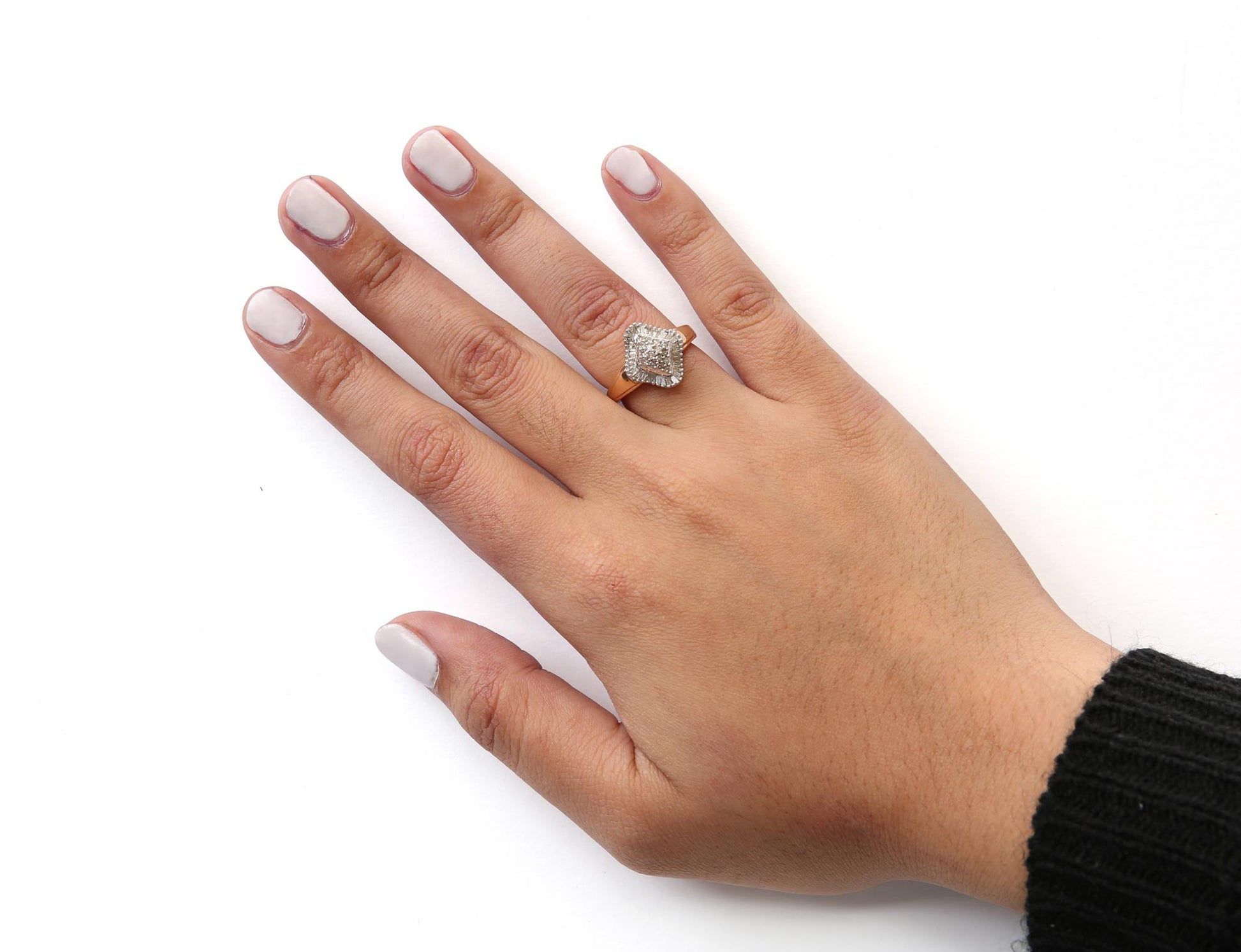 Yellow metal ring with white round and baguette gemstones, worn on a model’s hand, top-down angle.