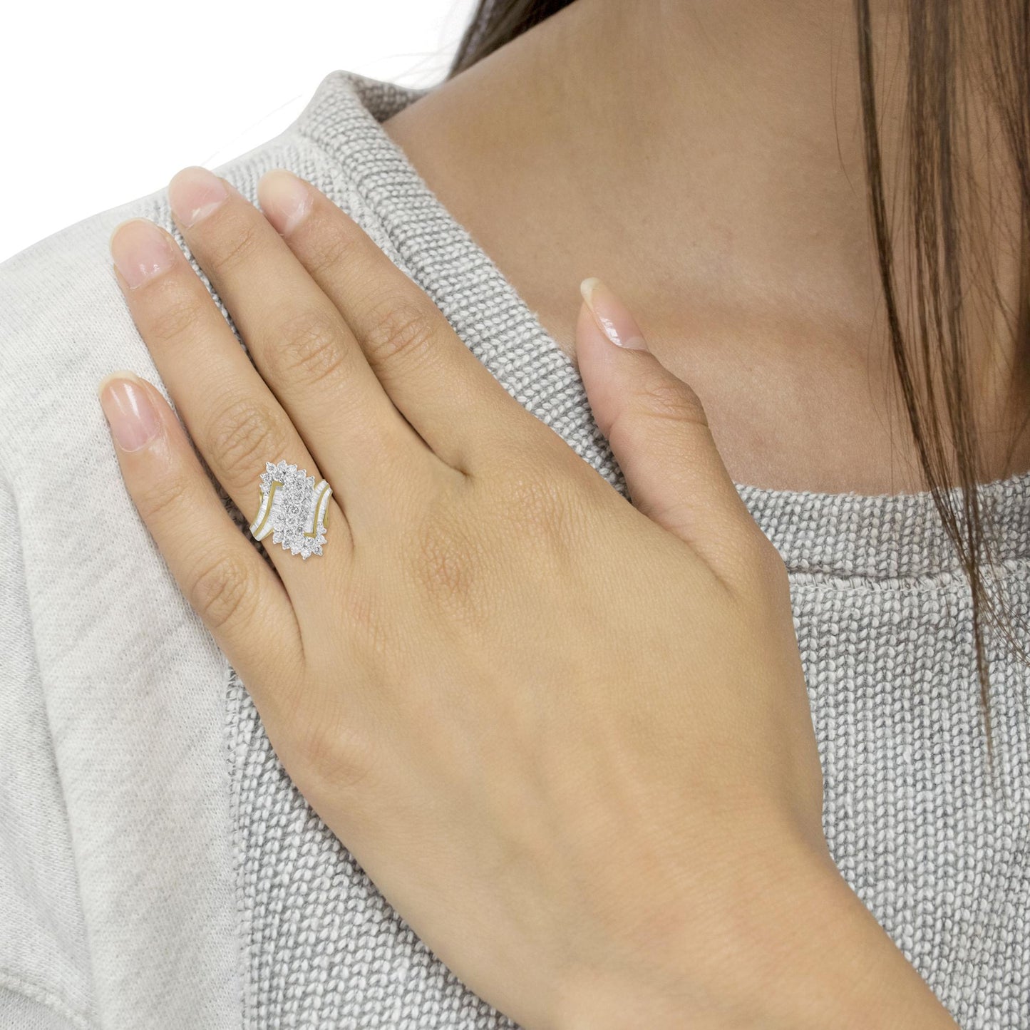 Close-up of a yellow ring with round prong-set white gemstones and baguette channel-set white gemstones, worn on a model's hand viewed from above.