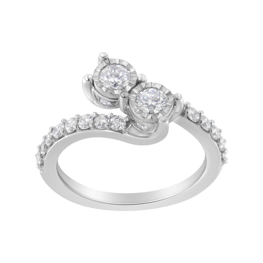 White metal ring with two round white gemstones in miracle setting and additional round white gemstones in prong setting along the band, shown in a close-up angled view.