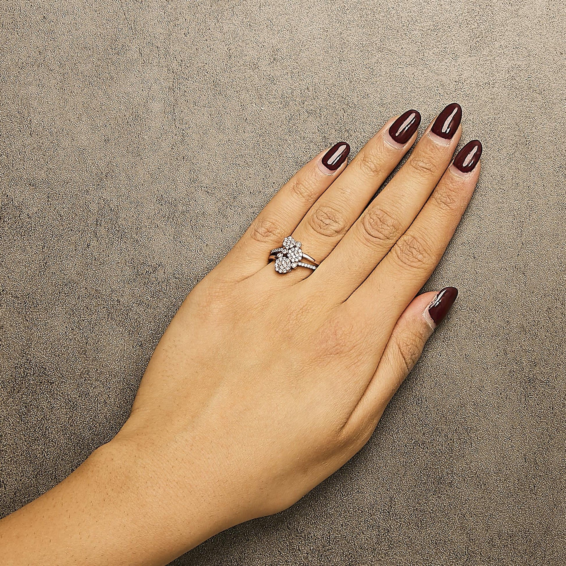 Rose-colored ring with multiple prong-set white round gemstones, worn on a model's hand, shown from above.