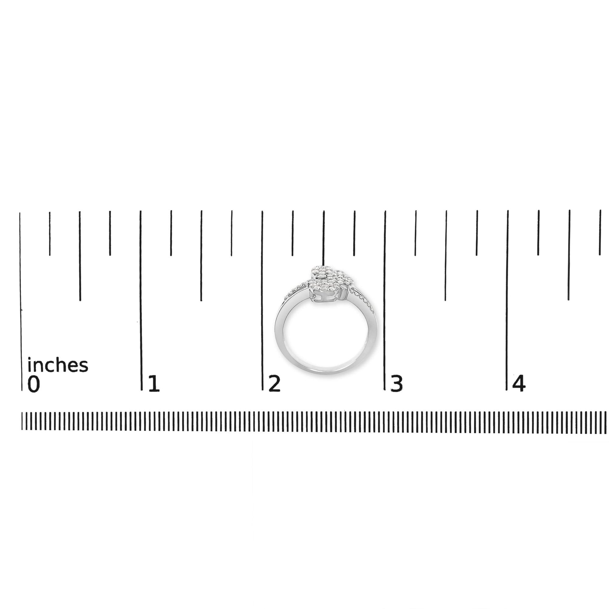 White metal ring with multiple round white gemstones in prong settings, viewed from the front on a ruler for size reference.