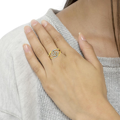 Yellow metal ring with intertwined design accented by round white gemstones in pave setting, shown on a model's hand from top angle.