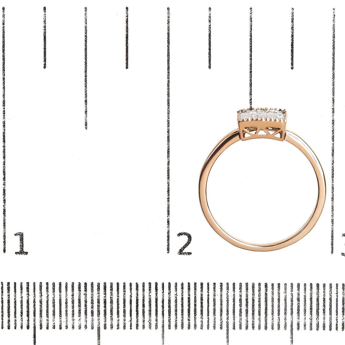 Rose metal ring with a row of white princess-shaped gemstones in an invisible setting, shown from the side on a ruler for size reference.